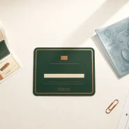 Editorial flat lay of a label roll with multiple bakery SKU designs, a finished forest green label and a flexible photopolymer printing plate on a warm white surface, representing the digital vs flexo label printing decision
