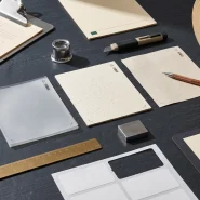 Materials engineer's evaluation bench with three sustainable label substrate samples, precision measurement tools and a production run sample sheet on a charcoal slate surface