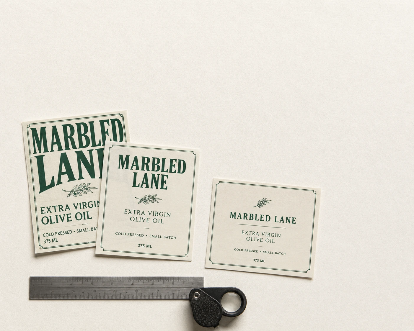 Three printed label revisions for the same product laid on paper with a steel rule and a jeweller's loupe
