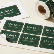 Print ready label artwork shown as a printed proof sheet with crop marks and spot colour swatches beside finished die cut labels on a liner