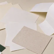 Sustainable label cost comparison: blank label material samples and a partially unwound adhesive label roll on a work counter